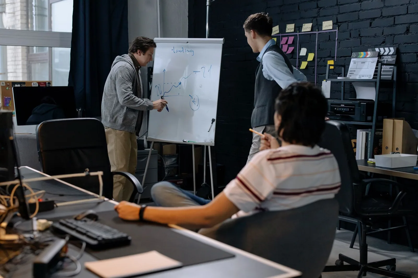 Two developers at a laptop reviewing a custom workflow diagram on a whiteboard in an office