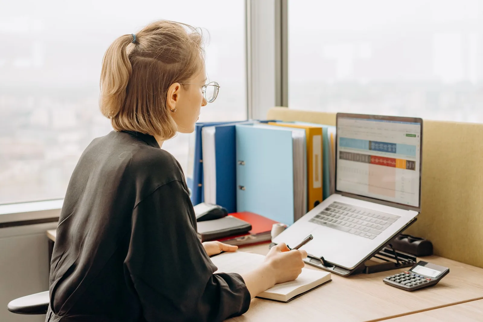 Small business founder reviewing workflow automation tasks on a laptop with spreadsheets and sticky notes