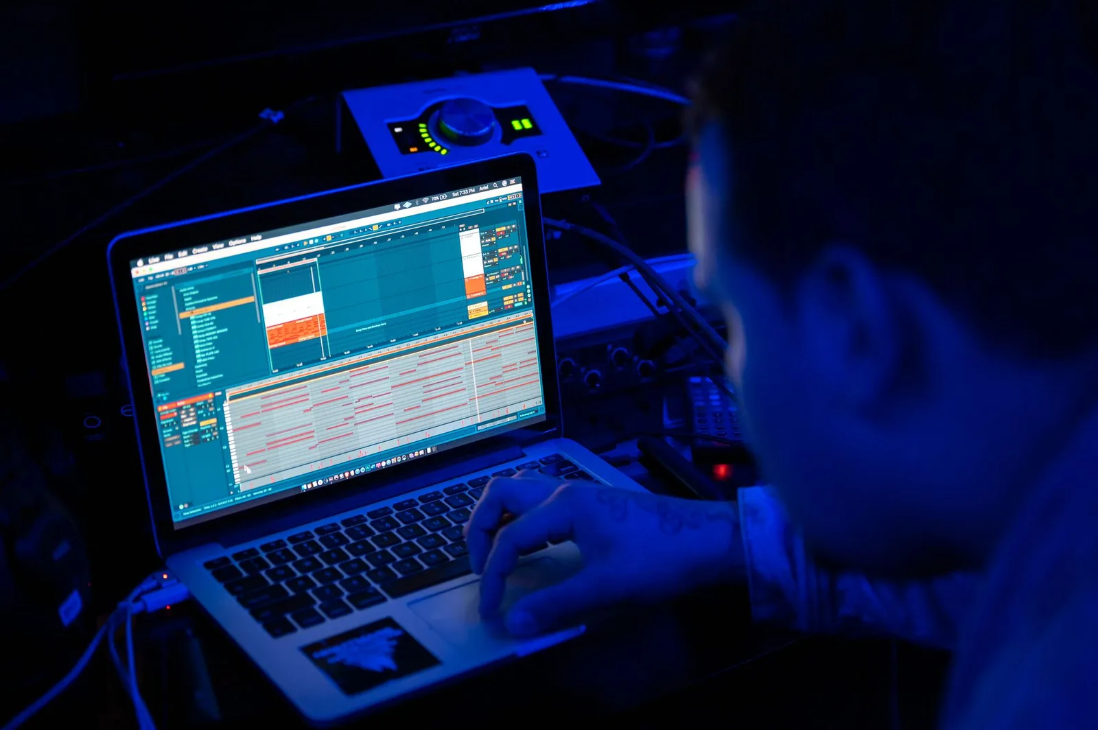 Developer reviewing code on a laptop terminal at night while background coding agents queue tasks